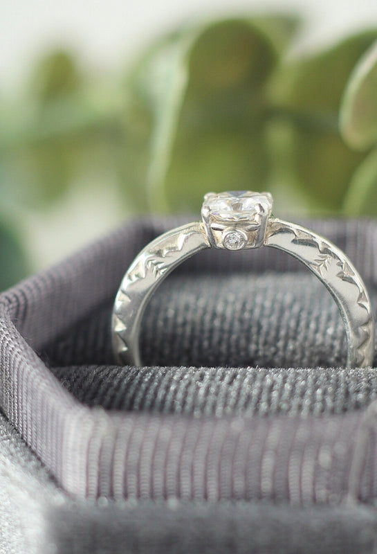 Side view of a white gold mountain engagement ring with a cushion cut moissanite stone and lab grown diamond details in hidden in the setting.