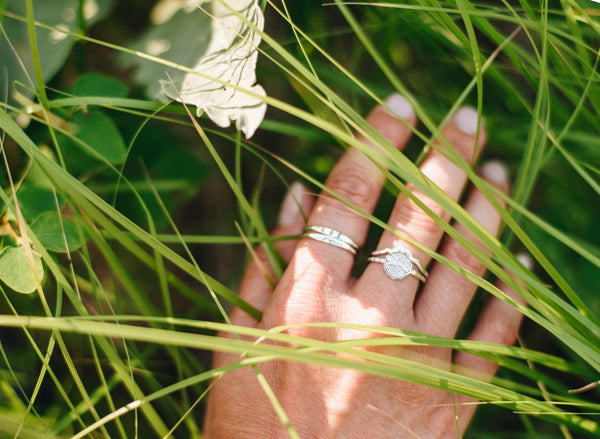 Silver mountain peaks ring on a woman's hand that is placed in tall meadow grass.