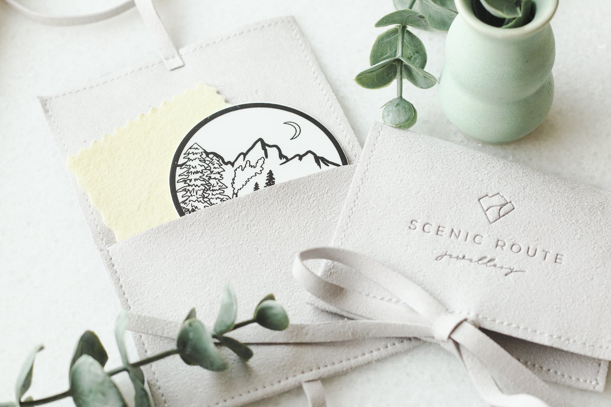 Scenic route jewellery vegan suede pouch showing off a mountain vinyl sticker and sunshine polishing cloth.