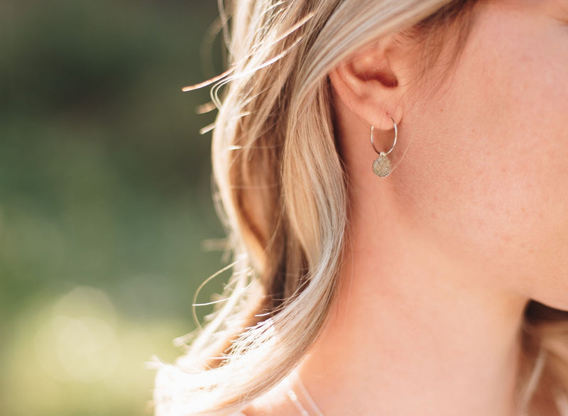 Woman in a forest wearing silver wire hoops with wood slice charms.