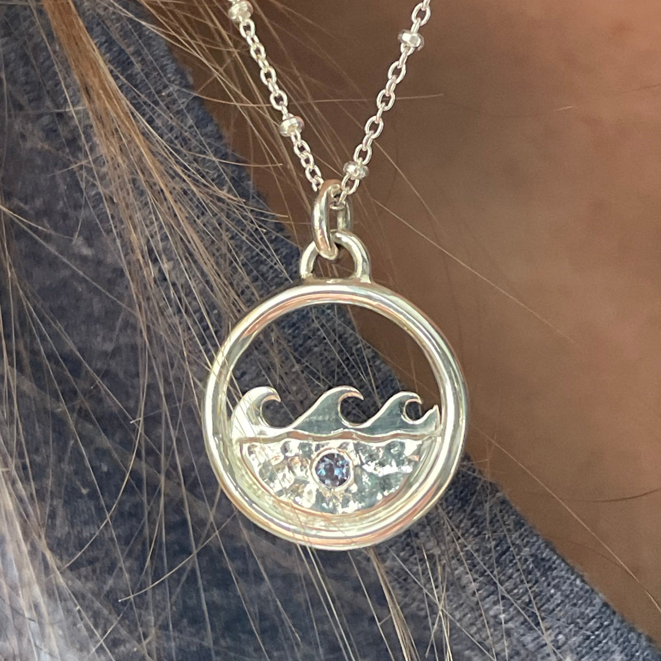 Necklace with a circular pendant featuring water and wave design with alexandrite, worn on a person's neck.