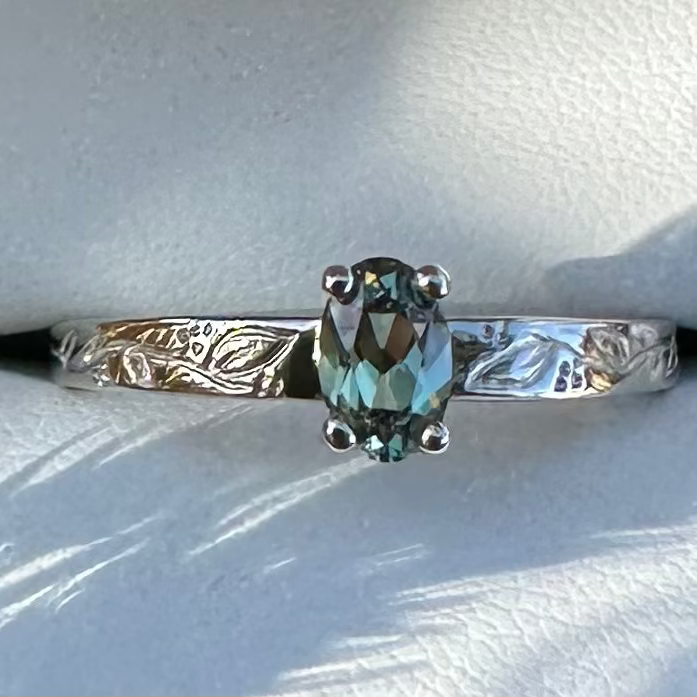 white gold ring with a green gemstone on a textured surface