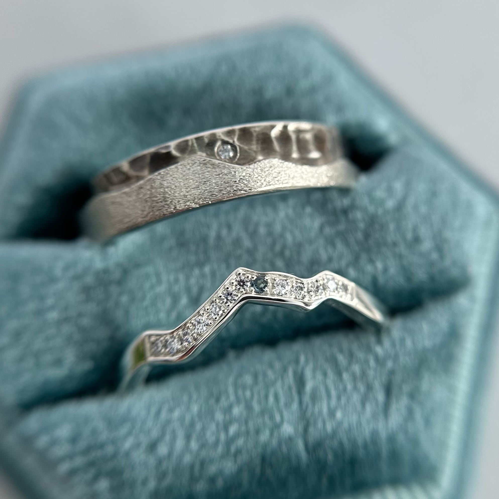 Two silver mountain rings with gemstones on a hexagonal blue velvet cushion.
