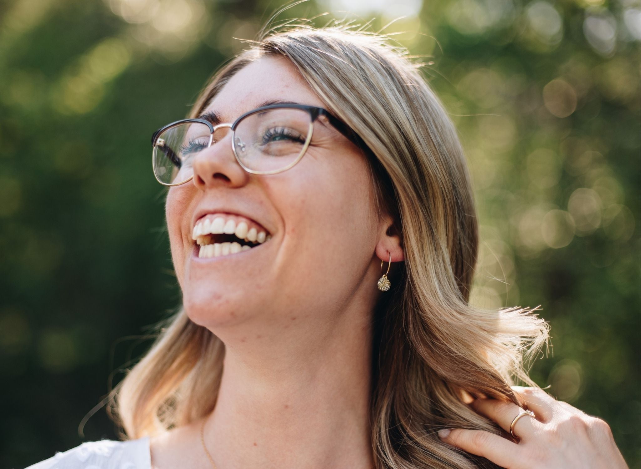 Woman in a forest wearing gold wire hoops with wood slice charms.