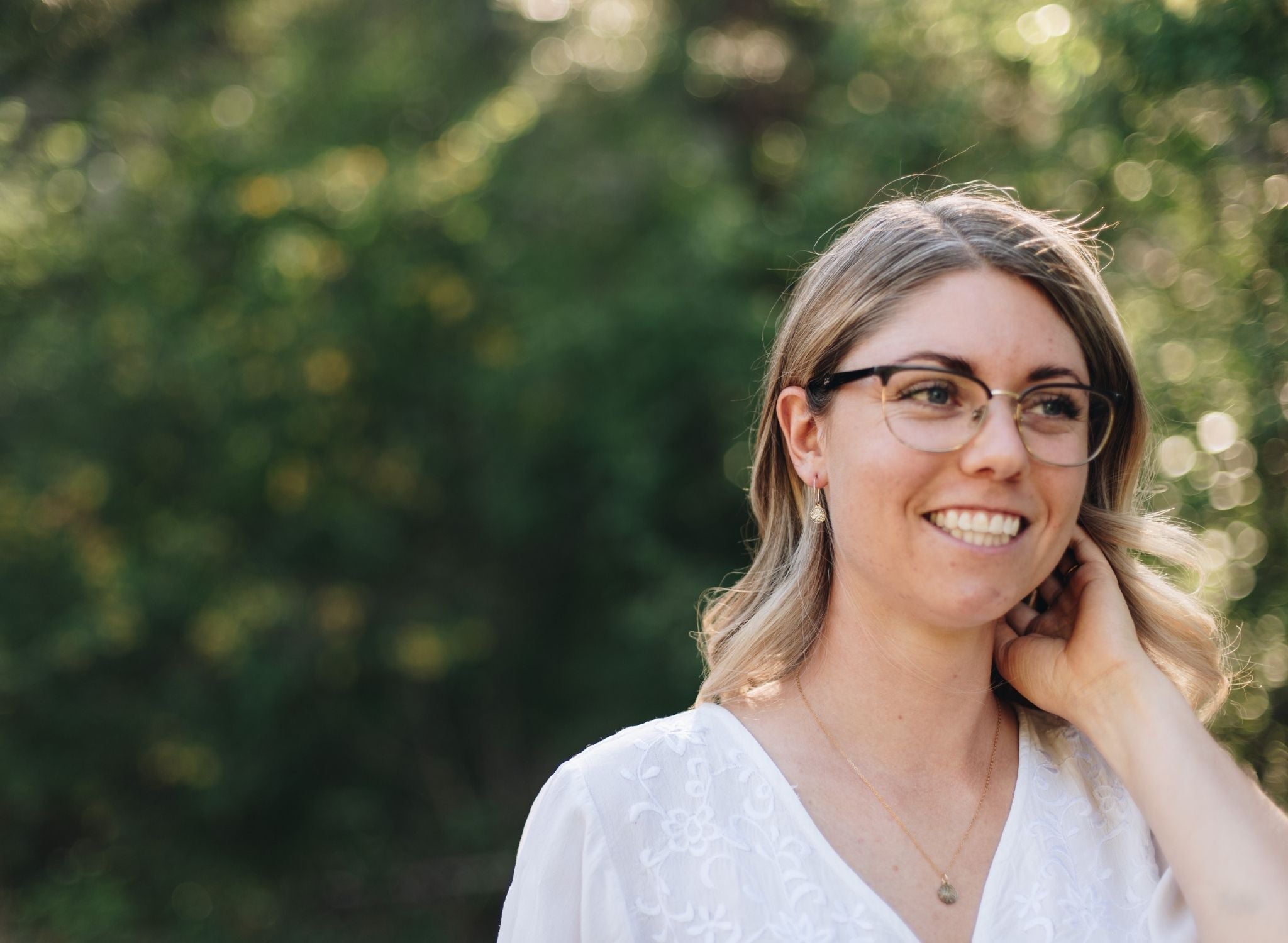 Woman in a forest wearing gold wire hoops with wood slice charms.