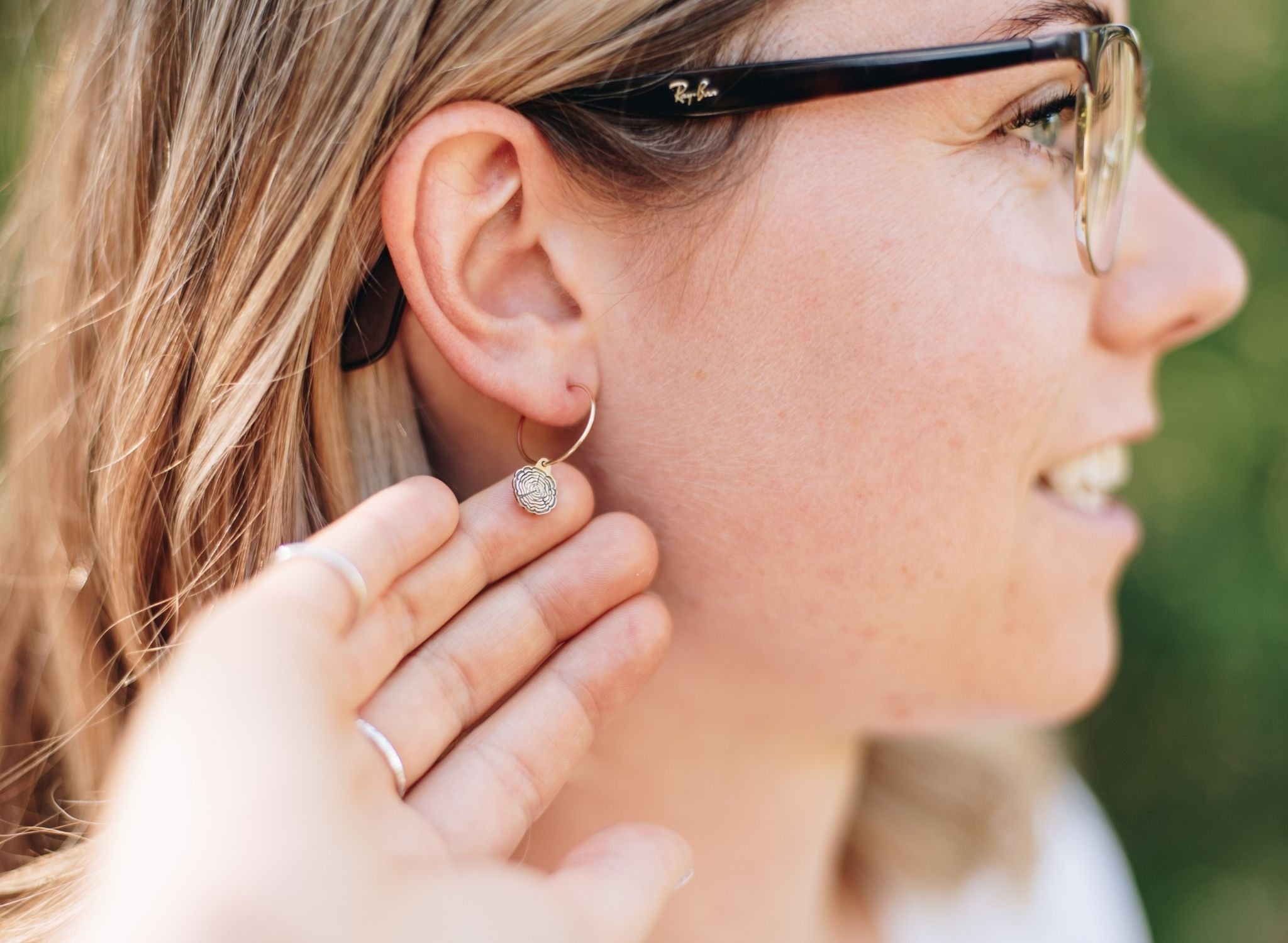 Woman in a forest wearing gold wire hoops with wood slice charms.