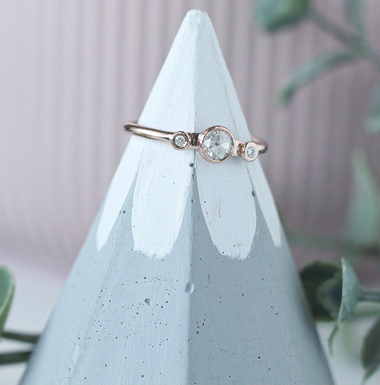 dainty rose gold ring featuring a round rose cut moissanite with melee moissanite on either side. 