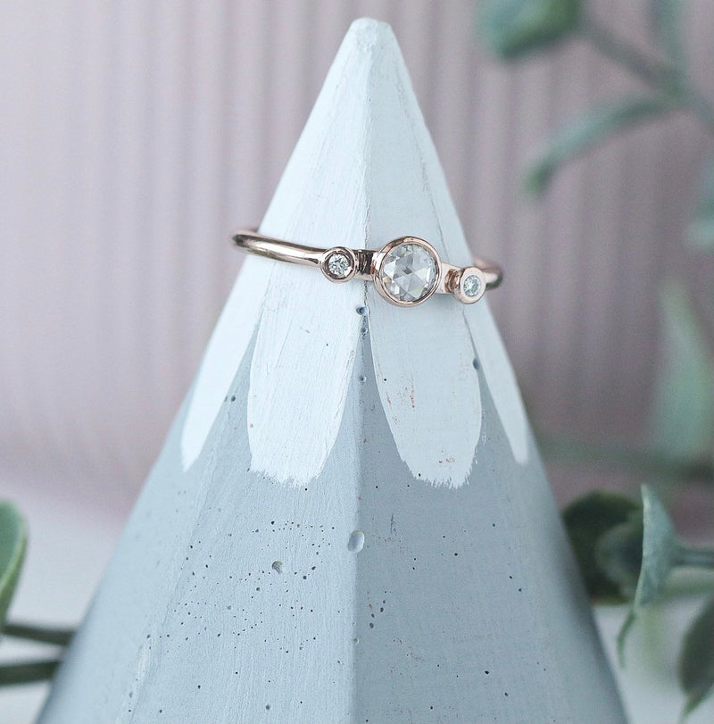 dainty rose gold ring featuring a round rose cut moissanite with melee moissanite on either side. 