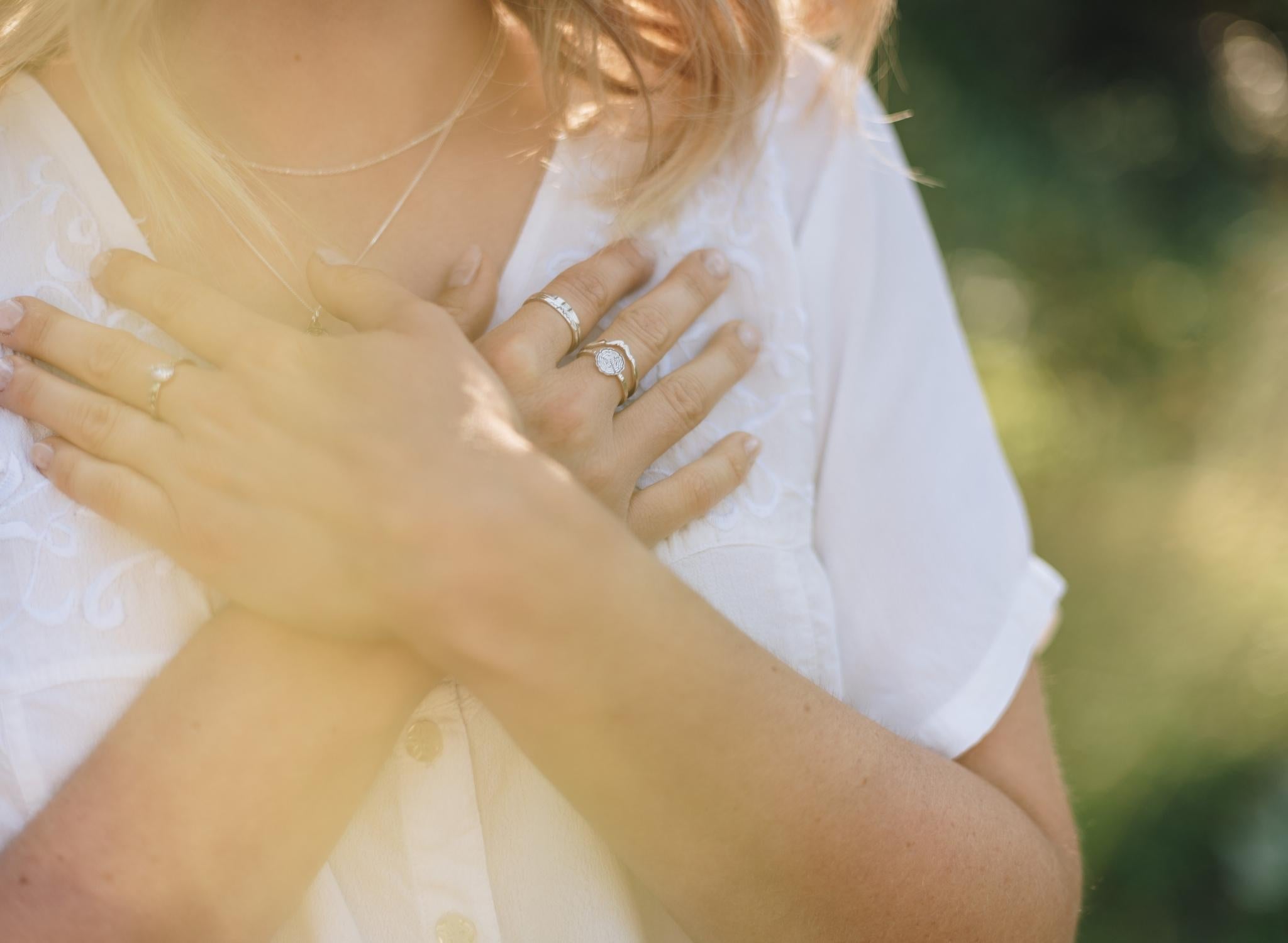 Woman in a green meadow holding her hands up on her chest. Her hands have silver nature inspired rings