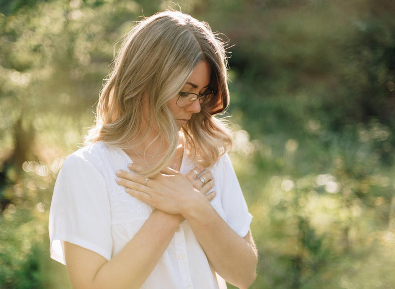 Woman in a green meadow holding her hands up on her chest. Her hands have silver nature inspired rings
