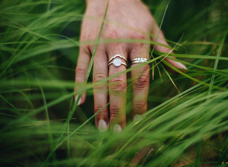 Collection of silver nature inspired rings on a hand in tall grass.