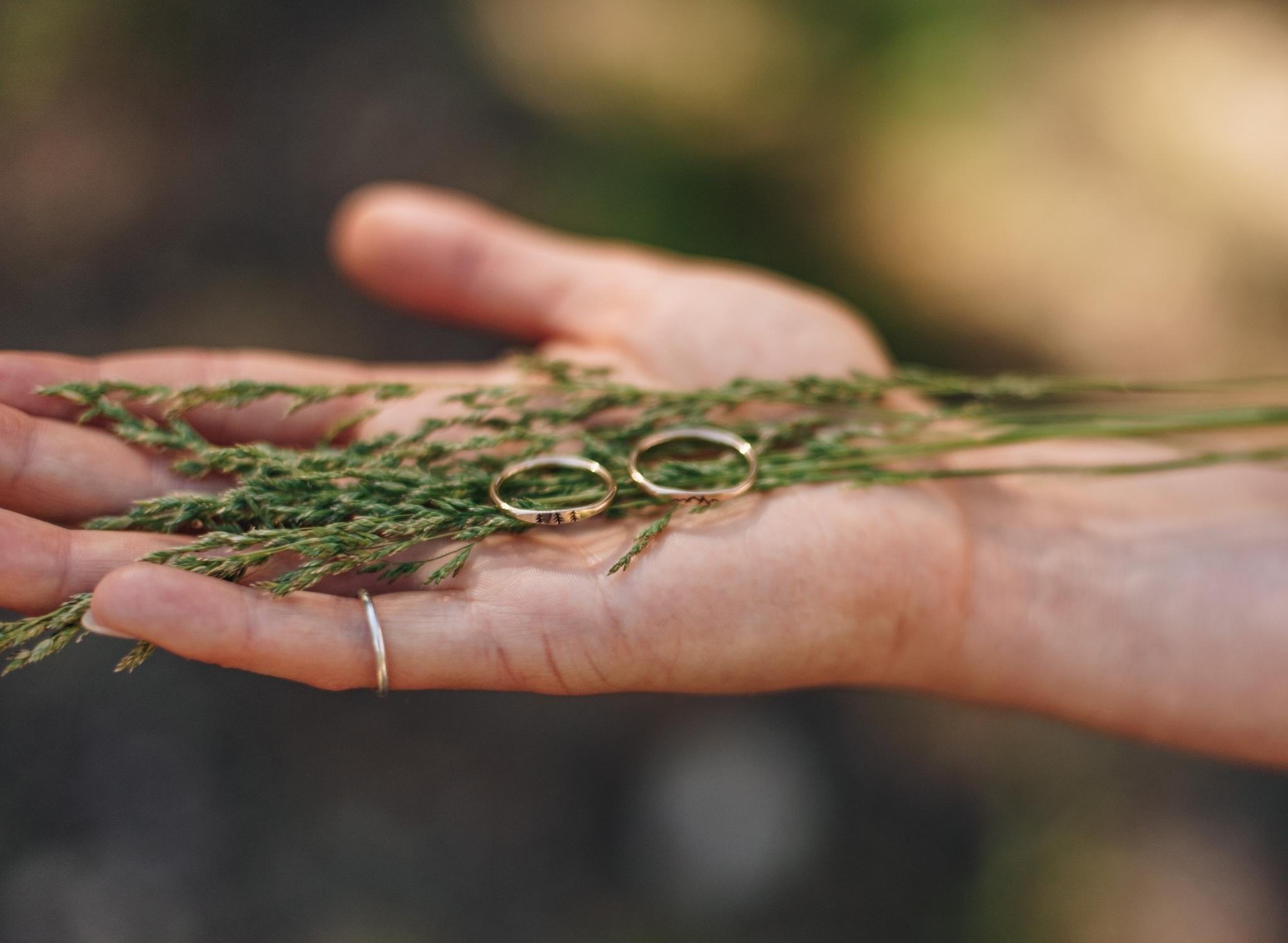 Woman's hand holding wheat and a tree and mountain ring on her palm.