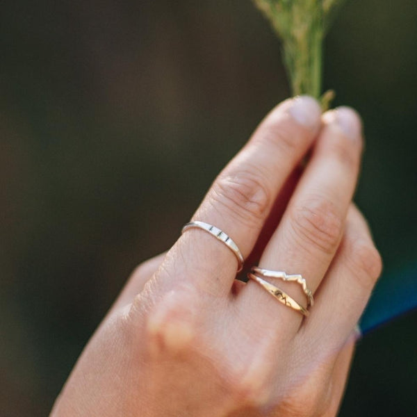 Woman's hand holding leaves with a silver tree ring on her pointer finger.