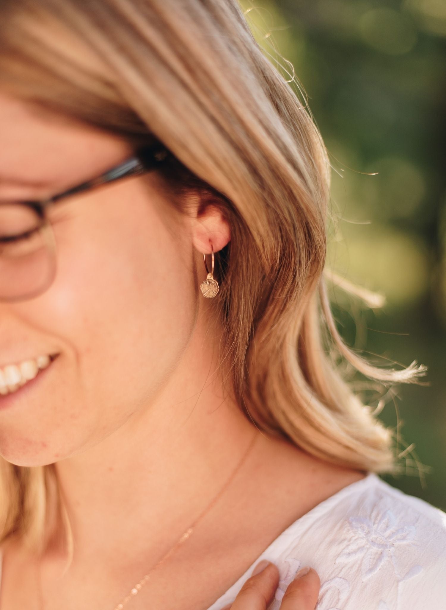 Woman in a forest wearing gold wire hoops with wood slice charms.