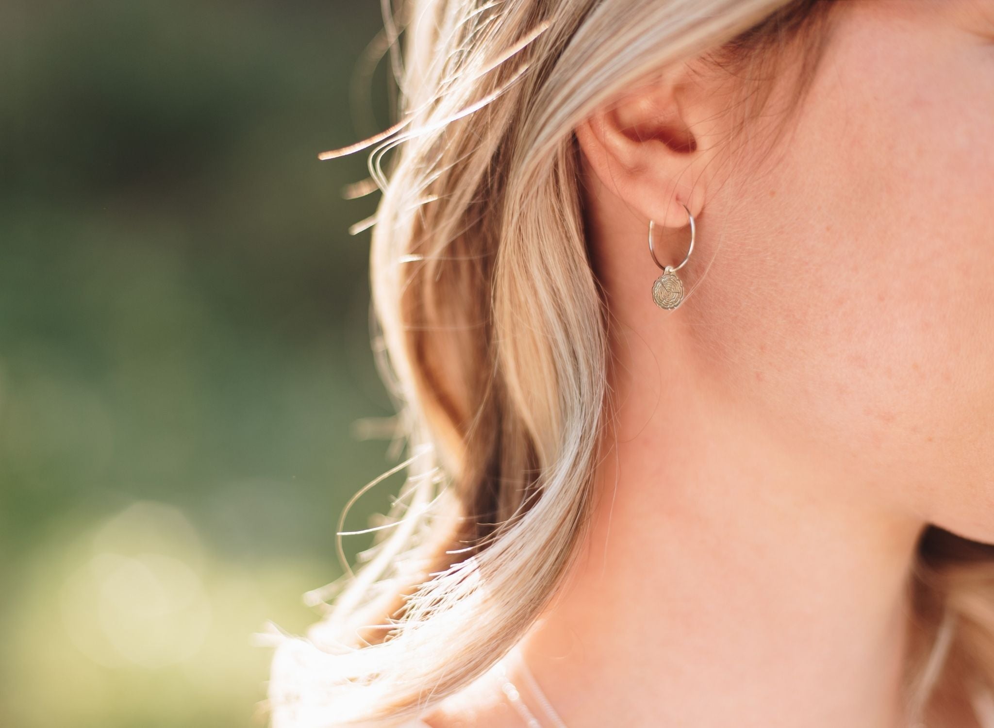 Woman in a forest wearing silver wire hoops with wood slice charms.